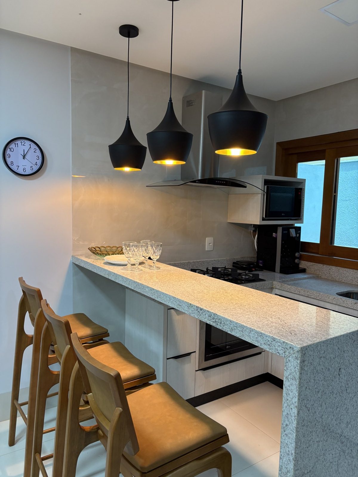 Cozinha completa e equipada dos chalés, com bancada em granito, cooktop, forno e banquetas
