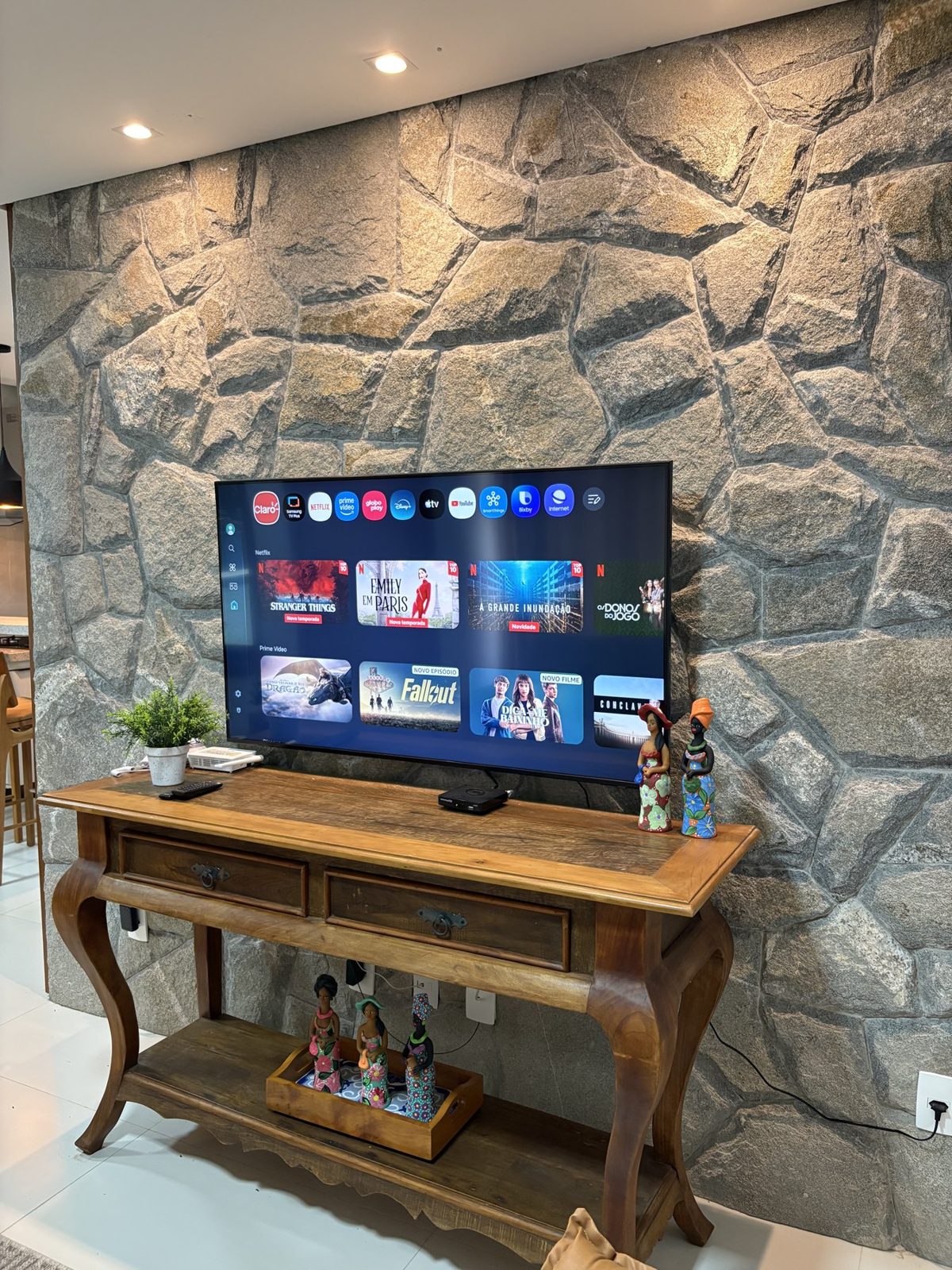 Sala de estar com parede de pedra, Smart TV, sofá e poltronas